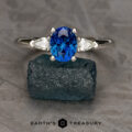 The "Avalon" ring in platinum, featuring a 1.46-carat Ceylon sapphire and two clear side stones, is displayed on a rough dark green stone, with "EARTH'S TREASURY" branding below.