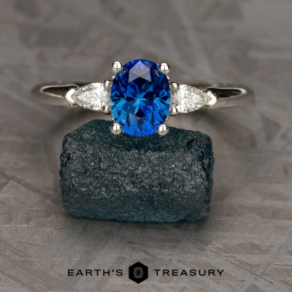 The "Avalon" ring in platinum with 1.46-carat Ceylon sapphire The "Avalon" ring in platinum, featuring a 1.46-carat Ceylon sapphire and two clear side stones, is displayed on a rough dark green stone, with "EARTH'S TREASURY" branding below.