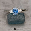 The "Alocasia" ring in 14K white gold features a 0.82-carat Montana sapphire and two clear side stones, displayed on rough blue crystal with the Earth's Treasury logo below.