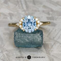 The "Chiron" ring in 18k yellow gold, featuring a 2.24-carat Montana sapphire and diamond accents, rests on a rough blue stone above the text "EARTH'S TREASURY," capturing celestial elegance.
