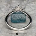 The "Selene" band in 18k white gold, featuring a rough blue gemstone and a Double Band Jacket, is photographed on a textured gray surface with the "Earth's Treasury" logo at the bottom.