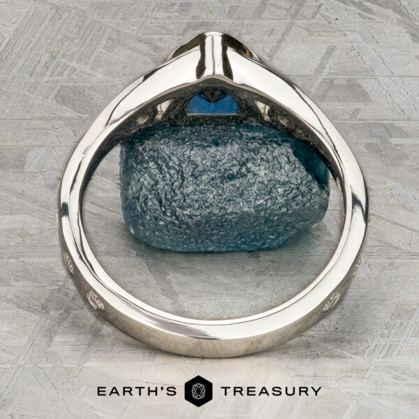 Foy, Andrew A close-up of the Foy, Andrew ring—a silver band with a blue gemstone—viewed from the side on a textured gray surface, with the "Earth's Treasury" logo beneath.