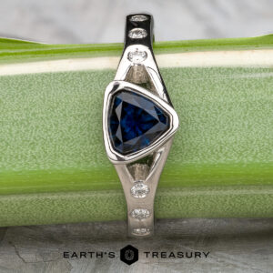 The "Corvus" Ring in platinum, set with a 1.00-carat Australian sapphire, is displayed on a green stem with the "EARTH'S TREASURY" logo beneath.