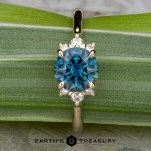 A gold Gaines, John (Jeremy) pendant with a round blue gemstone and six small diamonds, shown on a green leaf next to the Lipara Ring and the Earth's Treasury logo below.