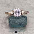 The "Selene" ring features a 1.11-carat Montana sapphire set in 14K rose gold, accented by two small round diamonds, and elegantly displayed on a rough blue stone.