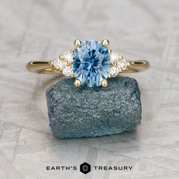 The "Kelli" ring in 18k yellow gold with 1.38-carat Montana sapphire The "Kelli" ring in 18k yellow gold with a 1.38-carat Montana sapphire is displayed on a rough blue stone. The text "EARTH'S TREASURY" is shown at the bottom.