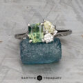 The "Moirae" ring in 14k white gold, featuring a 1.05-carat Australian sapphire, rests atop a rough blue stone on a textured gray surface. The Earth's Treasury logo is shown at the bottom.