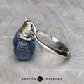 The "Moirae" ring in 14k white gold, featuring a 1.05-carat Australian sapphire, rests atop a rough blue stone on a textured gray surface. The Earth's Treasury logo is shown at the bottom.