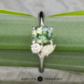 The "Moirae" ring in 14k white gold, featuring a 1.05-carat Australian sapphire, rests atop a rough blue stone on a textured gray surface. The Earth's Treasury logo is shown at the bottom.