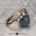 The "Solstice" ring in 14K yellow gold features a 0.90-carat Montana sapphire center stone with diamond accents, displayed on a blue-green mineral. The Earth’s Treasury logo appears below, evoking Solstice brilliance.