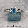 The "Corvus" ring in platinum with a 0.74-carat Montana sapphire is displayed on a rough blue stone, small diamonds accenting the rectangular blue gem, with the "Earth's Treasury" logo below.