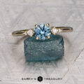 The "Selene" ring in 14K yellow gold, featuring a 0.98-carat Montana sapphire and two small diamonds, stands on a rough blue stone. The Earth's Treasury logo is visible at the bottom.