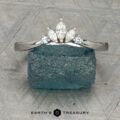 The "Alene" band in 14K white gold with an empty prong setting stands upright against a blue-green rough gemstone, with the Earth's Treasury logo visible at the bottom.