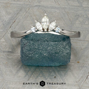 The "Alene" band in 14K white gold with an empty prong setting stands upright against a blue-green rough gemstone, with the Earth's Treasury logo visible at the bottom.