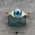 The Cathedral "Mavis" ring in 14K yellow gold features a 1.58-carat Montana sapphire flanked by two triangular diamonds, displayed on a rough blue crystal with the "Earth's Treasury" logo below.