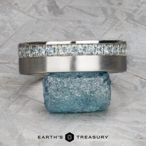 A platinum Linus Ring with a Montana sapphire is displayed balanced on a rough blue stone, with the text "Earth's Treasury" below.