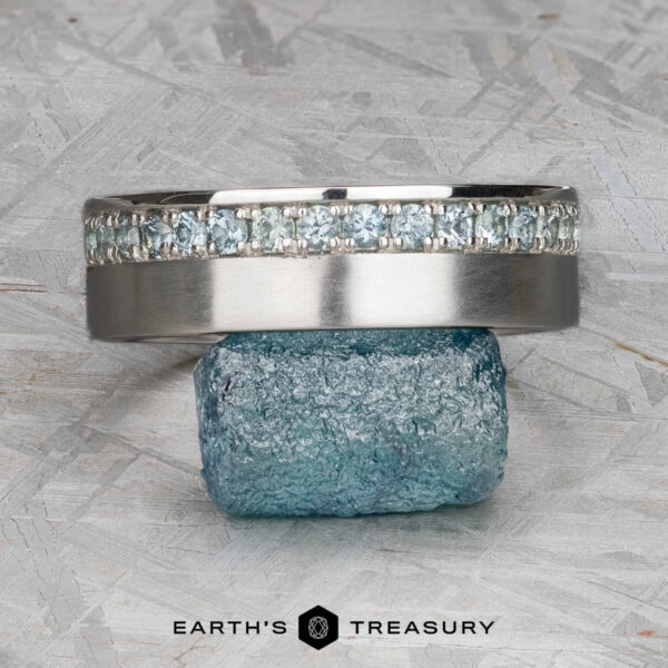 The "Linus" ring in platinum with Montana sapphire A platinum Linus Ring with a Montana sapphire is displayed balanced on a rough blue stone, with the text "Earth's Treasury" below.