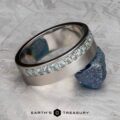A platinum Linus Ring with a Montana sapphire is displayed balanced on a rough blue stone, with the text "Earth's Treasury" below.