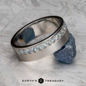 A platinum Linus Ring with a Montana sapphire is displayed balanced on a rough blue stone, with the text "Earth's Treasury" below.