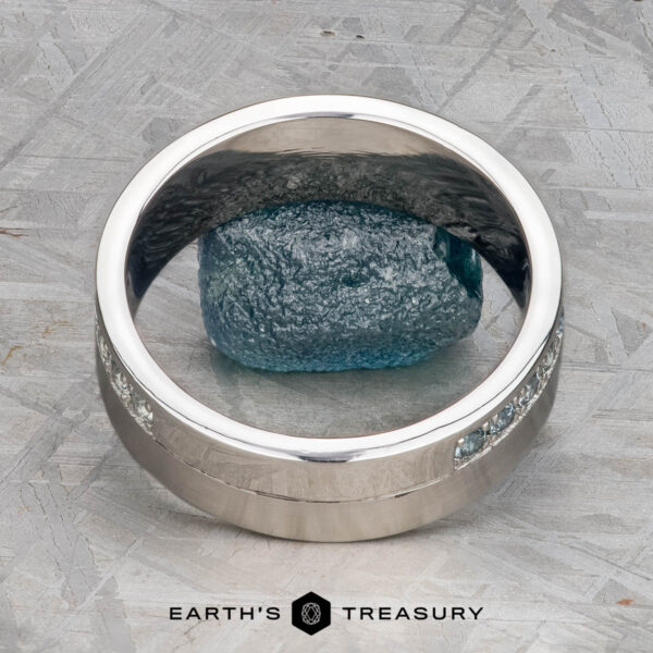 The "Linus" ring in platinum with Montana sapphire A platinum Linus Ring with a Montana sapphire is displayed balanced on a rough blue stone, with the text "Earth's Treasury" below.