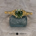 The "Guinevere" ring in 14k yellow gold with a 1.41-carat Australian sapphire from the Guinevere Solitaire collection is shown on a rough blue stone, with the "Earth's Treasury" logo and text at the bottom.