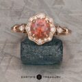 The "Cordelia" ring in 14K rose gold showcases a 1.38-carat Montana sapphire surrounded by small diamonds, set upright on a dark mineral rock with “Earth’s Treasury” branding below.