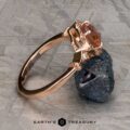 The "Cordelia" ring in 14K rose gold showcases a 1.38-carat Montana sapphire surrounded by small diamonds, set upright on a dark mineral rock with “Earth’s Treasury” branding below.