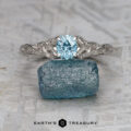 The "Guinevere" ring in 14k white gold with a 0.84-carat Montana sapphire rests atop a rough blue crystal on a textured gray surface, with the text "EARTH'S TREASURY" displayed below.