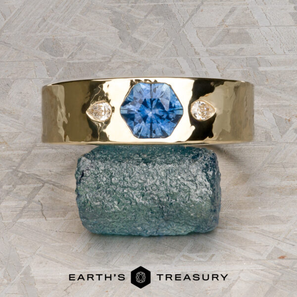 The "Hermes" ring in 14k yellow gold, hammered, with 0.99-carat The "Hermes" ring in hammered 14k yellow gold features a 0.99-carat blue gemstone at its center, flanked by two diamonds, and is elegantly displayed on a rough blue-green stone.