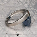 The "Declan" ring in platinum with a 1.02-carat Montana sapphire rests on a rough blue crystal atop a patterned metallic surface, with the "EARTH'S TREASURY" logo shown at the bottom.