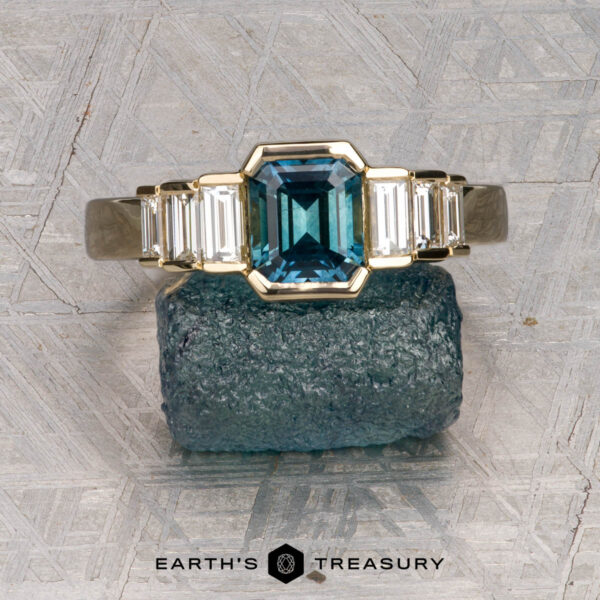 The "Apollo" ring in 14K yellow gold with 1.35-carat Montana sapphire The "Apollo" ring in 14K yellow gold with a 1.35-carat Montana sapphire is displayed on a rough crystal, with the "Earth's Treasury" logo below.