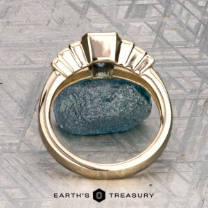 The "Apollo" ring in 14K yellow gold with a 1.35-carat Montana sapphire is displayed on a rough crystal, with the "Earth's Treasury" logo below.