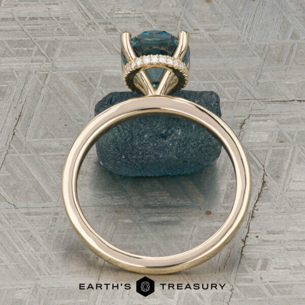 The "Aubrey" ring in 14K yellow gold with 3.37-carat Montana sapphire The "Aubrey" ring in 14K yellow gold, featuring a 3.37-carat Montana sapphire and hidden halo, is showcased on a rough blue stone atop a textured gray surface with the "Earth’s Treasury" logo below.