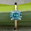 The "Aubrey" ring in 14K yellow gold, featuring a 3.37-carat Montana sapphire, is displayed upright against a green bamboo background.