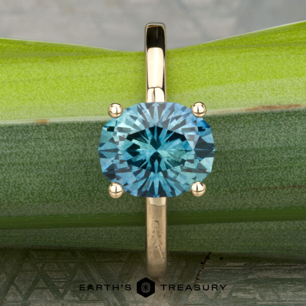 The "Aubrey" ring in 14K yellow gold with 3.37-carat Montana sapphire The "Aubrey" ring in 14K yellow gold, featuring a 3.37-carat Montana sapphire, is displayed upright against a green bamboo background.