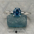 The "Ripple" ring in platinum, featuring a 1.23-carat Montana sapphire, is shown on a rough blue stone with a patterned gray background. "EARTH'S TREASURY" is displayed at the bottom.