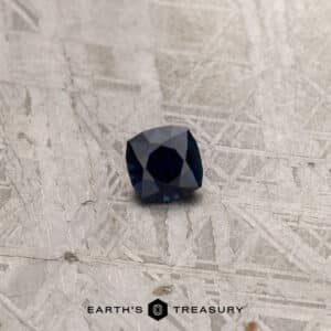 A square-cut, khaki green gemstone set on a light, textured surface with a geometric pattern. A logo and the text "Earth's Treasure" appear at the bottom center of the image.