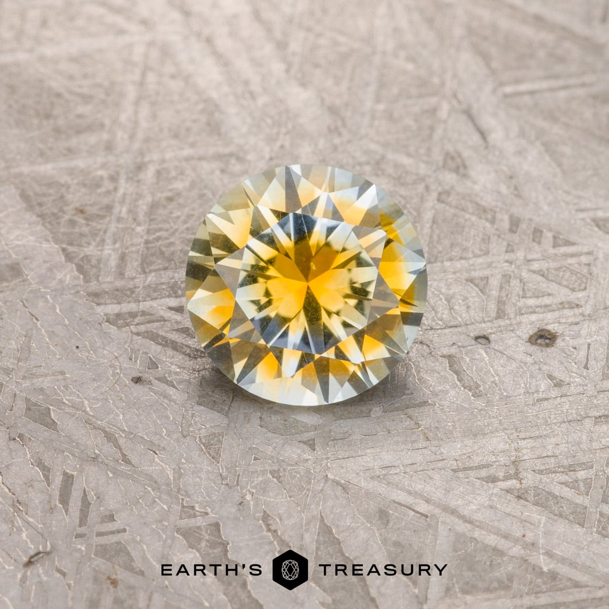 A 1.68-carat golden yellow-aqua particolored Montana sapphire is displayed on a textured surface with the label "Earth's Treasury" at the bottom, admired by countless customer testimonials.