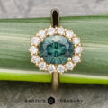 An 18k yellow gold "Cassandra" ring featuring a 1.79-carat Montana sapphire, encircled by clear diamonds, showcased on a green leaf with the "EARTH'S TREASURY" logo at the bottom.