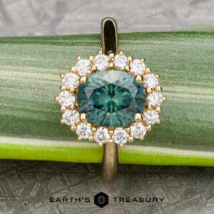 An 18k yellow gold "Cassandra" ring featuring a 1.79-carat Montana sapphire, encircled by clear diamonds, showcased on a green leaf with the "EARTH'S TREASURY" logo at the bottom.