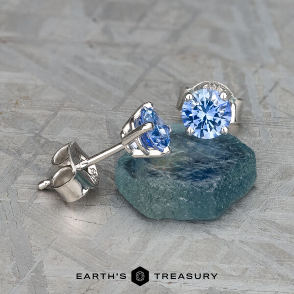 The EA-DB-402 earrings elegantly feature medium blue sapphires, each gemstone adding a sophisticated touch, beautifully set on a textured silver surface.