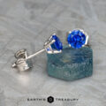 The EA-DB-403 earrings are a stunning pair featuring blue sapphire gemstones measuring 3.5-5.0 mm, set in silver, elegantly displayed on a textured surface and teal block.