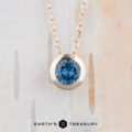 The FJ-NEC-101 4.5mm gold bezel slide necklace features a round teal blue gemstone pendant, showcased against a light, textured background. "EARTH'S TREASURY" is displayed at the bottom.