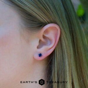 Close-up of a woman's ear adorned with 5mm deep blue earrings; "Earth's Treasury" logo and text appear at the bottom.