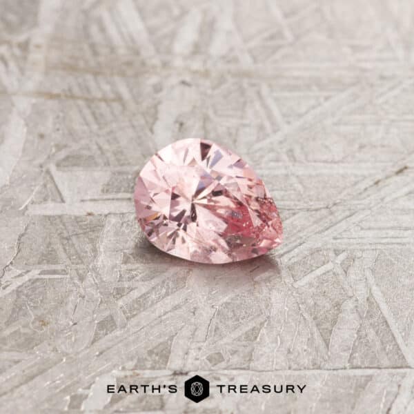 A 1.12-Carat Padparadscha Pink Ceylon Sapphire, expertly faceted into a pear shape, rests on a textured surface with a metallic and scratched appearance. The text "EARTH'S TREASURY" is prominently displayed at the bottom of the image.