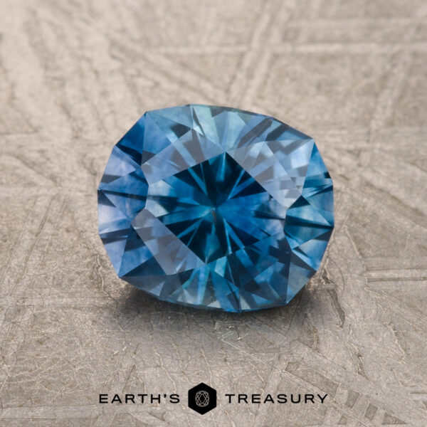 1.67-Carat Medium Blue Montana Sapphire (Heated) A 1.67-carat medium blue heated Montana Sapphire is displayed on a textured surface with the Earth's Treasury logo and name at the bottom.