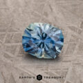 A 1.27-carat blue-aqua particolored Montana Sapphire with a round, geometric cut is displayed on a textured gray surface, featuring the text "Earth's Treasury" at the bottom.