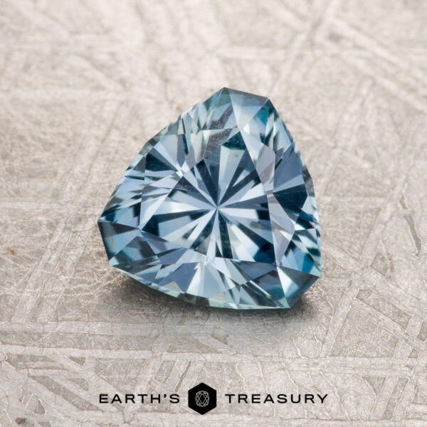 1.25-Carat Light Aqua Blue Montana Sapphire A 1.25-Carat Light Aqua Blue Montana Sapphire, trillion-cut and faceted, is displayed on a textured surface with the "Earth's Treasury" logo and text beneath it.