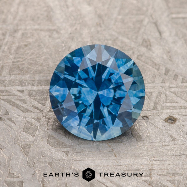 1.31-Carat Medium Blue Montana Sapphire (Heated) A 1.31-carat medium blue heated Montana Sapphire is shown on a textured gray surface with "EARTH'S TREASURY" below.