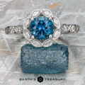The “Paeonia” Ring in platinum with a 1.68-carat Montana Sapphire and a diamond halo rests on a rough blue crystal atop a textured gray surface, with the Earth’s Treasury logo below.